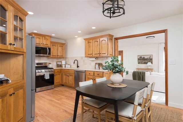 kitchen with light wood-style flooring, a sink, decorative backsplash, light countertops, and appliances with stainless steel finishes