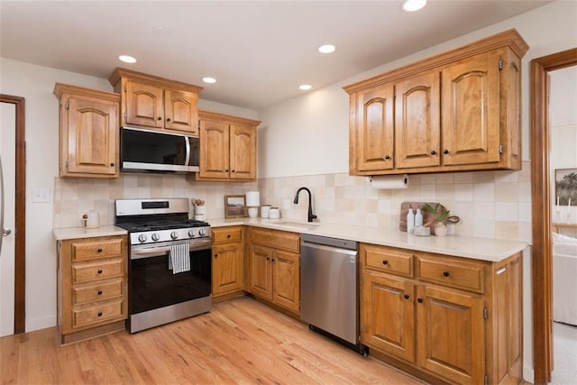 kitchen featuring a sink, decorative backsplash, light countertops, stainless steel appliances, and light wood-style floors