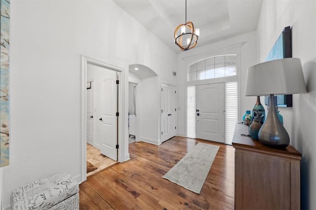 entrance foyer featuring baseboards, arched walkways, a raised ceiling, a towering ceiling, and wood finished floors