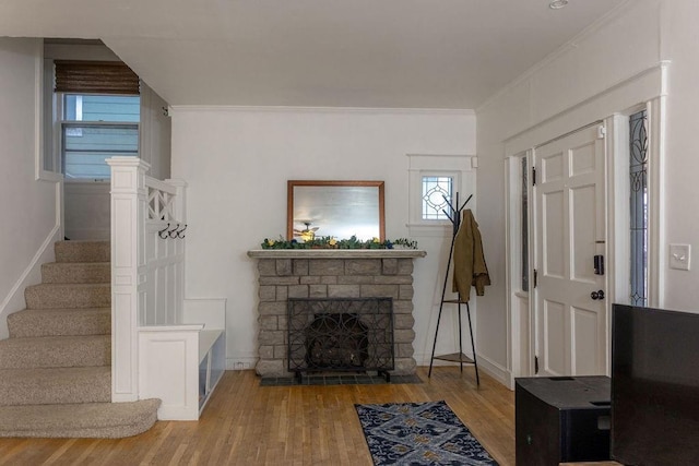 living area with a fireplace, wood finished floors, baseboards, stairway, and crown molding