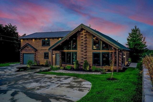 view of front facade with metal roof, a garage, concrete driveway, a lawn, and a standing seam roof