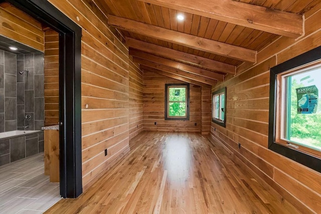 empty room featuring a healthy amount of sunlight, wooden ceiling, wooden walls, and lofted ceiling with beams