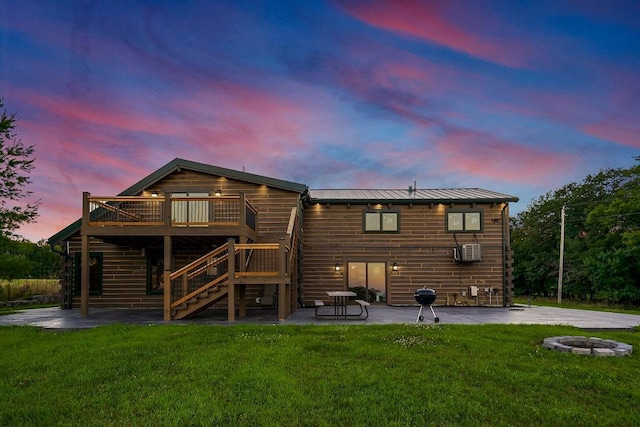 back of property at dusk with a deck, a patio area, a yard, and stairway