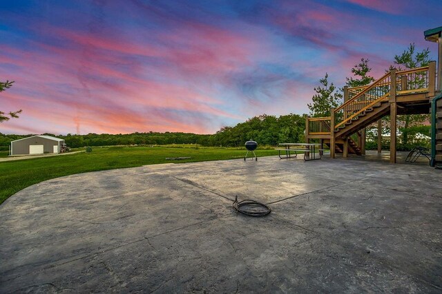 patio terrace at dusk with a garage, a yard, stairway, and a deck