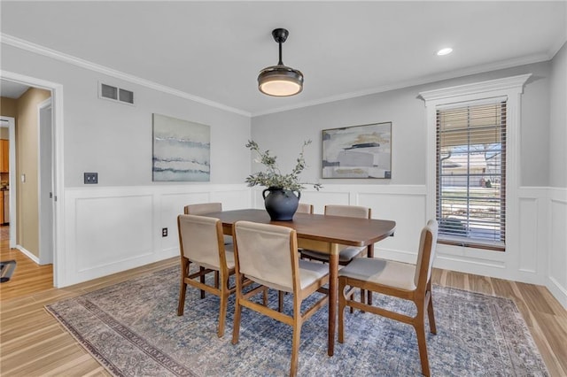 dining space featuring visible vents, light wood-style flooring, ornamental molding, wainscoting, and a decorative wall