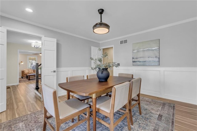 dining room with visible vents, light wood-style floors, a wainscoted wall, and crown molding