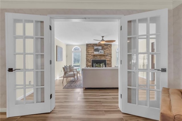 living room featuring wood finished floors, ceiling fan, a stone fireplace, french doors, and crown molding