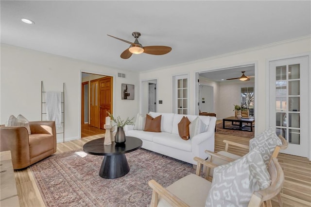 living room with ceiling fan, visible vents, light wood-style flooring, and crown molding