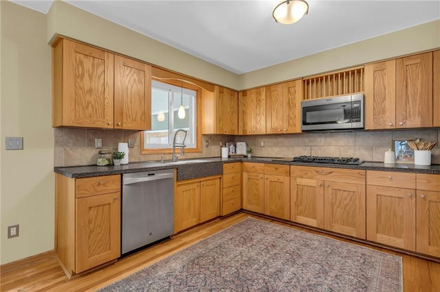 kitchen featuring stainless steel appliances, dark countertops, decorative backsplash, and light wood finished floors