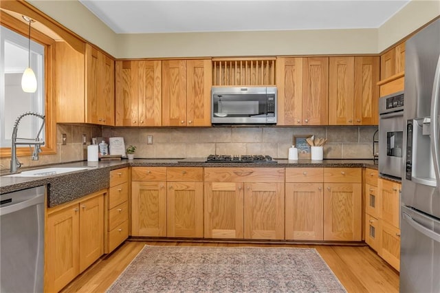 kitchen with decorative backsplash, light wood finished floors, appliances with stainless steel finishes, and a sink