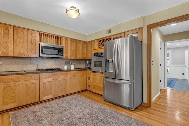 kitchen featuring visible vents, light wood-style flooring, decorative backsplash, appliances with stainless steel finishes, and wainscoting