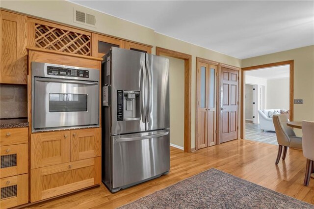 kitchen featuring visible vents, light wood-style floors, appliances with stainless steel finishes, dark countertops, and backsplash