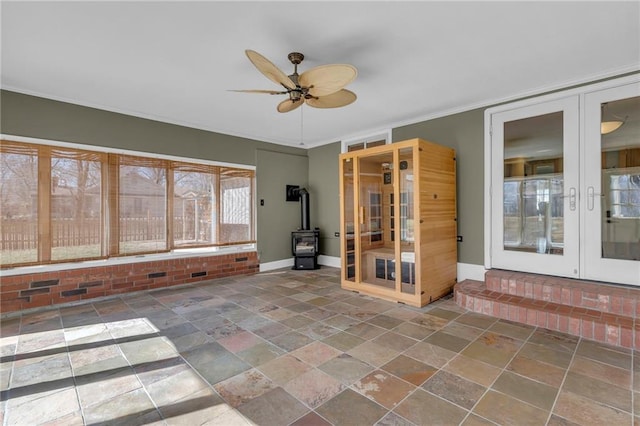 empty room featuring stone finish flooring, baseboards, a ceiling fan, and a wood stove