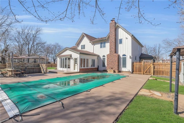 back of property with fence, board and batten siding, a fenced in pool, a chimney, and a patio area