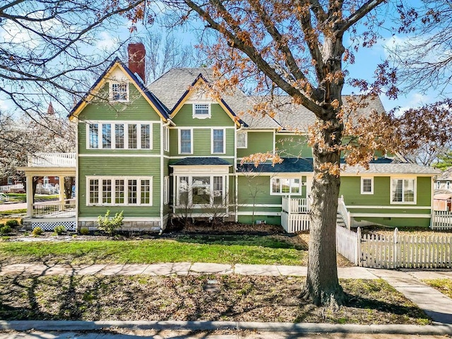 back of house with a shingled roof, a chimney, and a fenced front yard