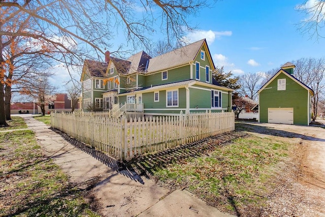 view of side of property with a garage, a fenced front yard, and an outbuilding