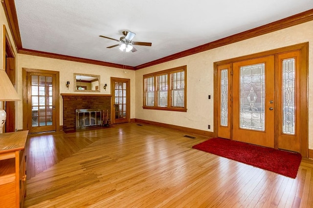 entrance foyer featuring ceiling fan, light wood-style flooring, baseboards, ornamental molding, and a brick fireplace