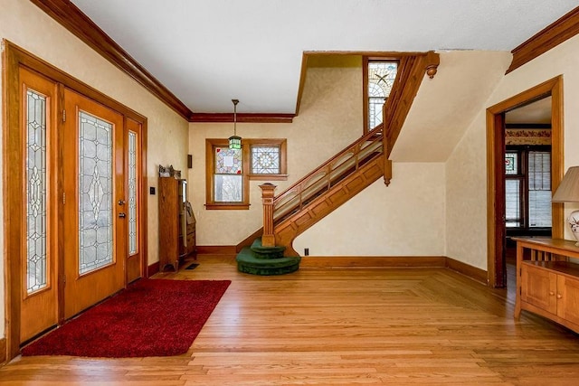 foyer with light wood finished floors, baseboards, stairway, and crown molding