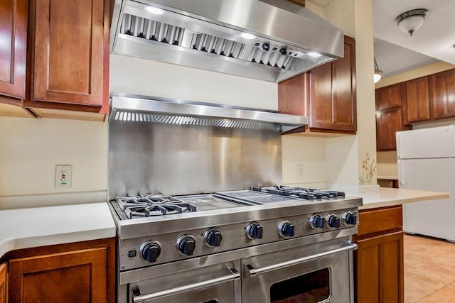 kitchen with range with two ovens, light countertops, wall chimney range hood, freestanding refrigerator, and brown cabinets