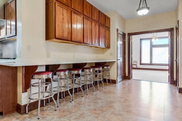 kitchen with baseboards, brown cabinets, hanging light fixtures, light countertops, and a kitchen bar