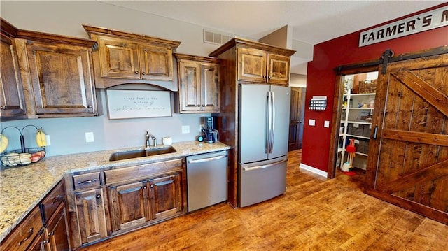 kitchen featuring a barn door, a sink, visible vents, appliances with stainless steel finishes, and light wood-type flooring