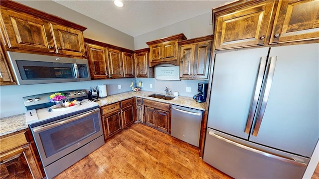 kitchen featuring stainless steel appliances, light wood finished floors, a sink, and light stone countertops