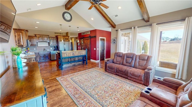 living area featuring lofted ceiling with beams, a barn door, wood finished floors, and a wealth of natural light