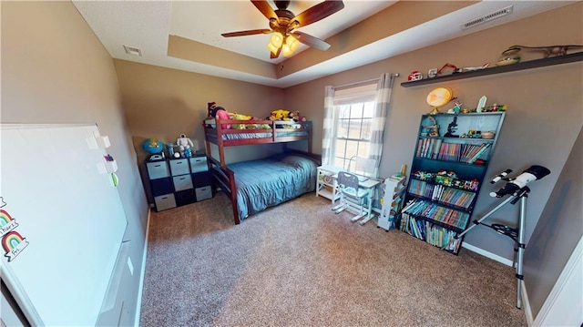 bedroom with a tray ceiling, visible vents, and carpet