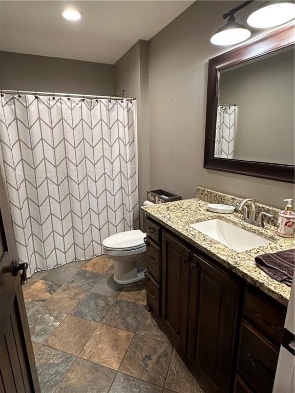 full bathroom featuring toilet, a shower with shower curtain, vanity, and stone tile floors