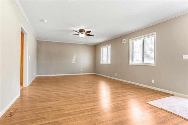 spare room with light wood finished floors, visible vents, ornamental molding, a textured ceiling, and a ceiling fan