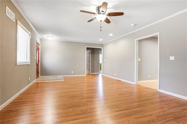 empty room featuring light wood-type flooring, baseboards, visible vents, and crown molding