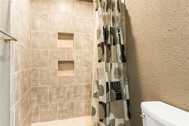 bathroom with toilet, a tile shower, and a textured wall