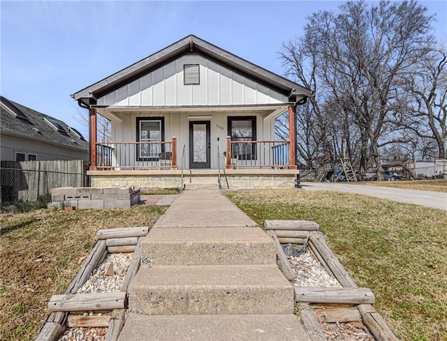 bungalow-style house with a front lawn, fence, covered porch, and board and batten siding