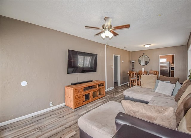 living room with a ceiling fan, wood finished floors, baseboards, and a textured ceiling