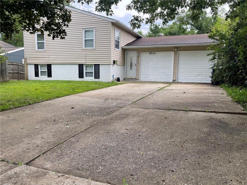 8641 E 97th Ter, Kansas City, MO 64134 - split level home featuring driveway, an attached garage, fence, a front lawn, and brick siding