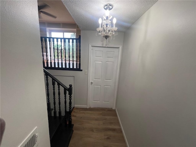 doorway to outside with a textured ceiling, wood finished floors, visible vents, baseboards, and an inviting chandelier