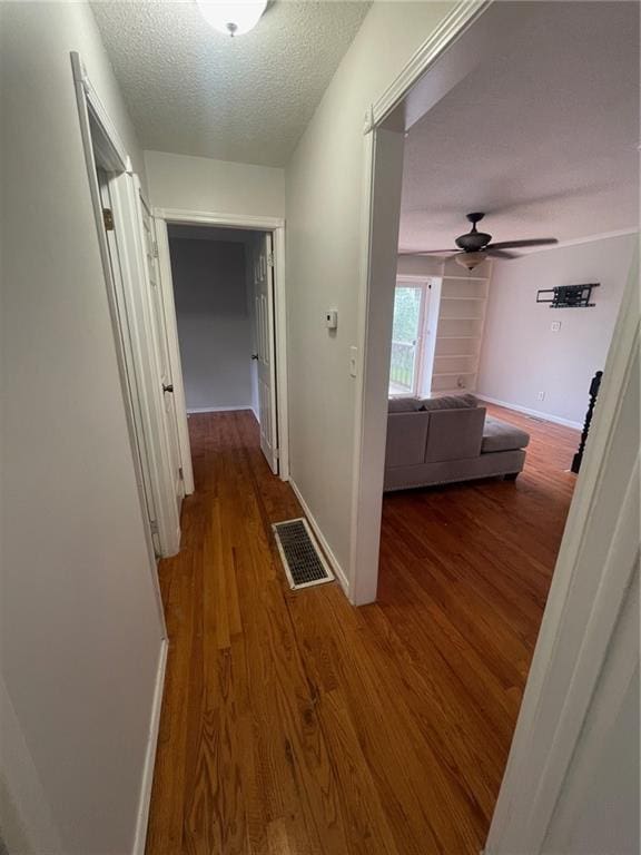 corridor featuring baseboards, a textured ceiling, visible vents, and wood finished floors