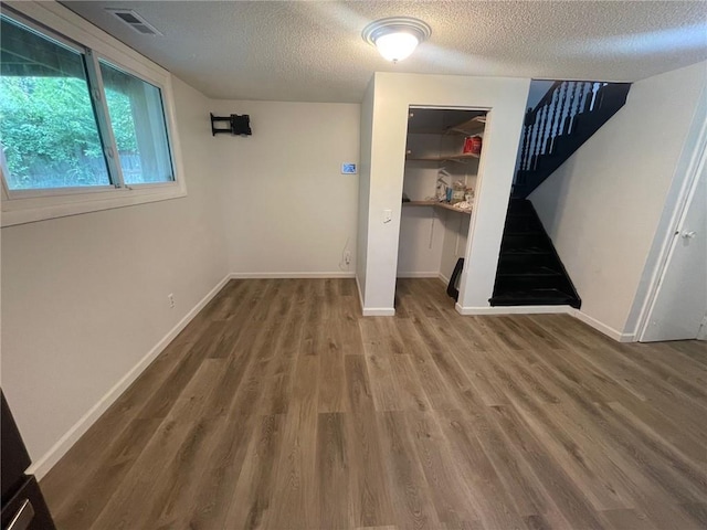 interior space featuring a textured ceiling, wood finished floors, visible vents, baseboards, and stairway