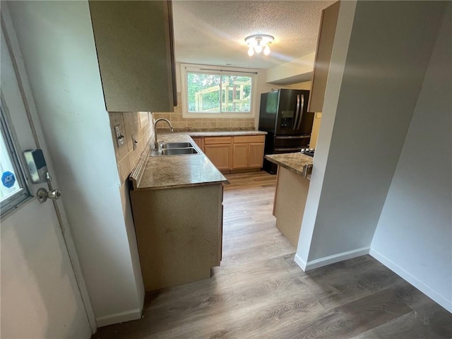 kitchen featuring light wood finished floors, black fridge with ice dispenser, a sink, a textured ceiling, and backsplash