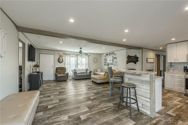 kitchen with dark wood-style flooring, open floor plan, white cabinetry, beamed ceiling, and a kitchen bar