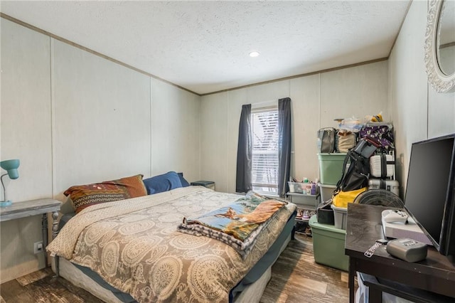 bedroom featuring a decorative wall, a textured ceiling, and wood finished floors