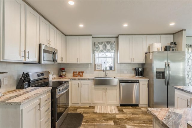 kitchen featuring tasteful backsplash, wood finished floors, stainless steel appliances, white cabinetry, and a sink