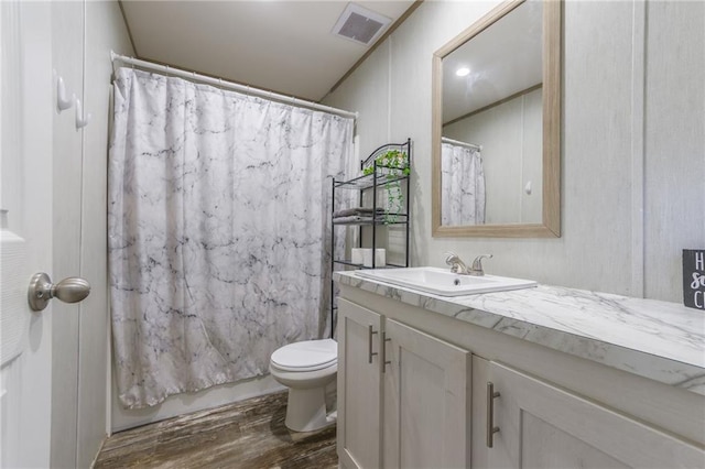 bathroom with toilet, vanity, wood finished floors, and visible vents