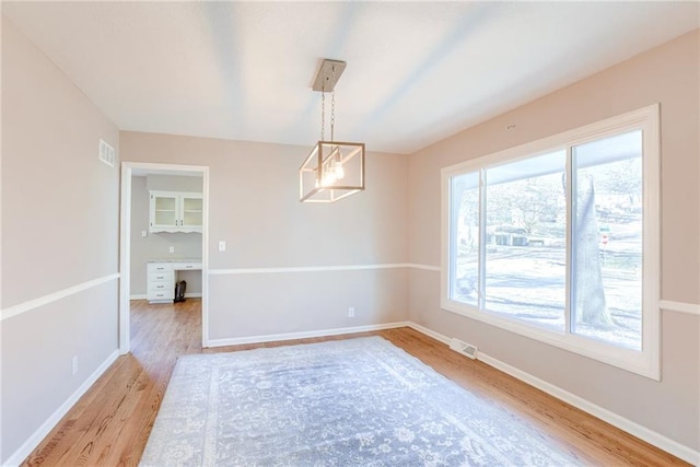 spare room with baseboards, visible vents, light wood finished floors, and an inviting chandelier