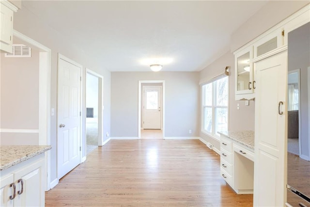 interior space featuring light wood-style flooring, glass insert cabinets, visible vents, and light stone countertops