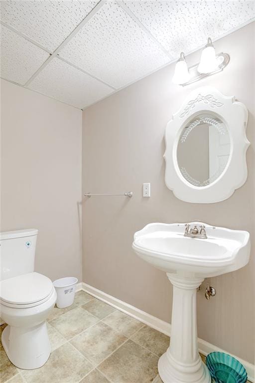 bathroom featuring a paneled ceiling, baseboards, toilet, and tile patterned floors