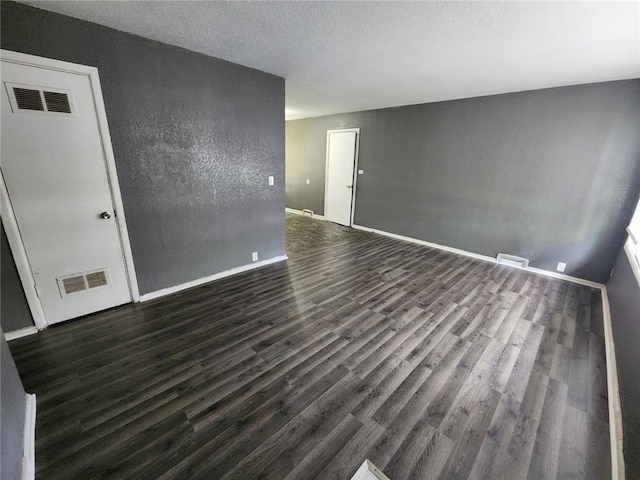 unfurnished room with a textured ceiling, dark wood finished floors, and visible vents