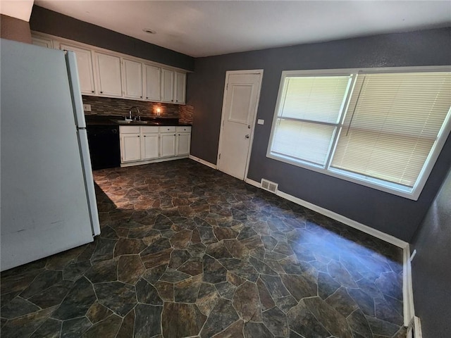 kitchen featuring dark countertops, visible vents, backsplash, freestanding refrigerator, and stone finish flooring