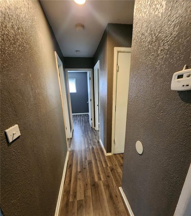 corridor with baseboards, dark wood finished floors, and a textured wall