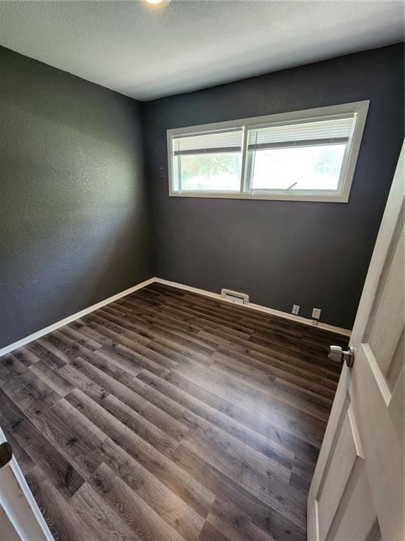 spare room featuring dark wood-style flooring, a textured wall, baseboard heating, a textured ceiling, and baseboards